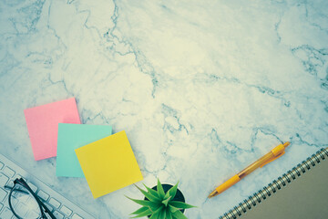 Modern Top View Office Desk or Office Table and Office Supplies as Stick Note or Notepad,Computer Keyboard,Pen,Spiral Notebook,Office Plants,Glasses on Marble Minimalist Background in Vintage Tone