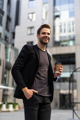 Closeup confident business man drinking coffee to go in city. Portrait of beautiful man looking away. Serious businessman waiting client on street