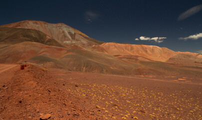 Travel and explore. Driving along the dirt road across the mountain arid desert. View of the route, red land, volcanic landscape, valley and mountains, very high in the Andes cordillera.