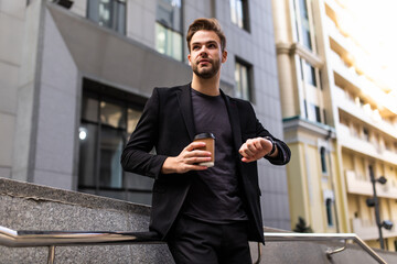 What time is it. Professional handsome businessman going to work while checking time holding coffee to go in the morning