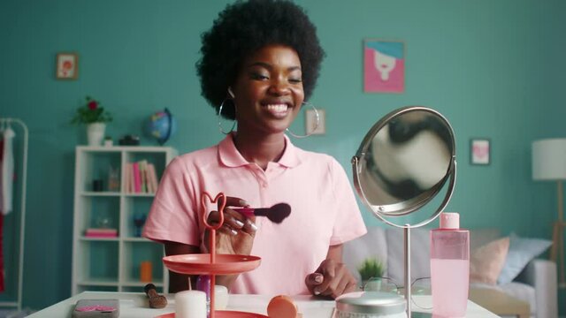 Young black woman is sitting at beauty table at home, getting ready to go outside, doing makeup, smiling at mirror and sending positive vibes to herself, Foreground, Slow motion.