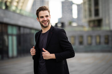 Modern businessman. Confident young man in full suit adjusting his sleeve and looking away while standing outdoors with cityscape