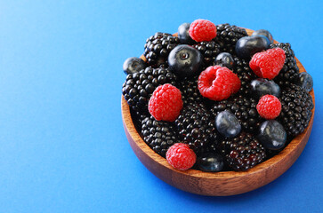 Fresh berries salad in a wooden plate on blue background. Flat lay, top view