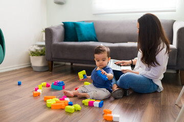 Baby playing with blocks and mother working on laptop