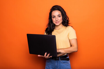 Surprised young woman working on laptop pc isolated on orange background. People sincere emotions...