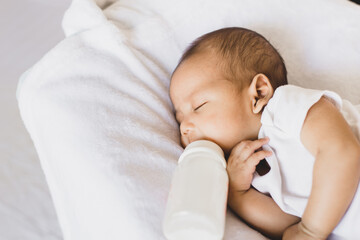 Adorable little asian newborn baby sleeping and drinking milk on a comfortable bed