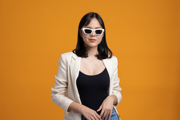 Attractive Beautiful asian woman standing and posing. Sexy female in suit wearing sunglasses on isolated yellow background.