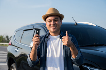 Young handsome asian man getting the new car.He showing car key and very happy. Buy or rent a car concept.