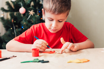 Cute 7 years old child boy paints wooden dinosaur toy for Christmas tree