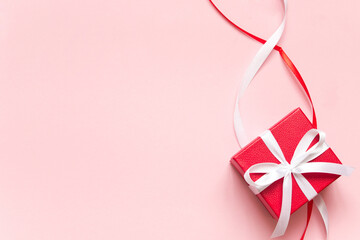 Red gift box with white ribbon and bow and red and white decorative ribbon on pink background. Concept of giving present, love, valentines day. Copy space, flatly