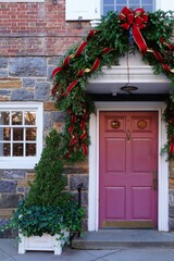 Christmas holiday pine garland with pinecones and red bow on a red door
