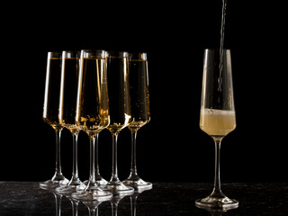 Five glasses of wine and one filling glass on a black background.