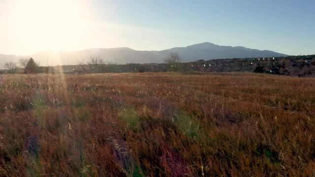 Sunset flight over grass field towards houses Pikes Peak Colorado 4K