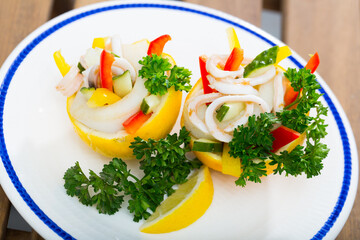 Tropical salad with calamaries, cucumbers and bell pepper served in lemon shells with dressing from olive oil and Greek yogurt