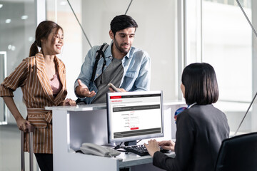 Couple of passengers talking to airline staff at check-in counter.