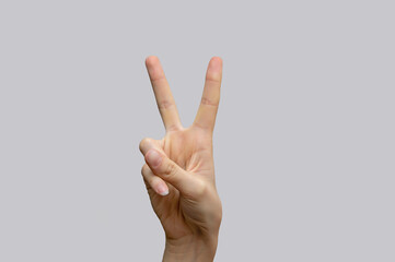 A white female hand showing the victory and peace sign on a light gray, isolated background. Close-up, selective focus, copy space