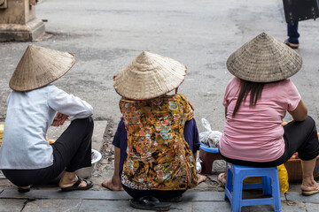 Three unidentifiable ladies selling food on the streets of Hanoi