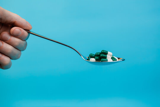 Human hand holding a tablespoon with colored pills. Closeup. Space for text. Pharmacology and medicine struggle for health. Medicine and health concept