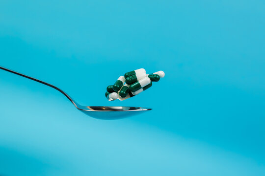 Colored pills falling on a tablespoon on a blue background. Closeup. Space for text. Pharmacology and medicine struggle for health. Medicine and health concept