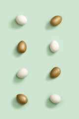 Pattern from Painted Easter eggs white and gold colored on light green paper. Minimal easter concept.