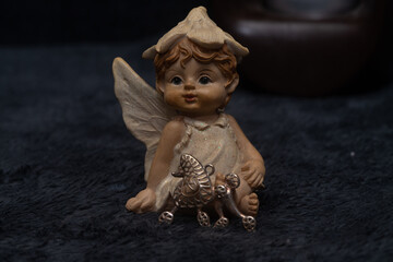 Figurine of a baby angel and a silver pendant in the shape of a poodle dog on the dark gray surface