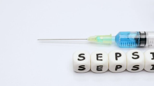 Slow panning on word sepsis spelt with white plastic cubes with a drug vial and syringe on white background. Sepsis awareness concept.