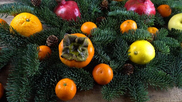 Abies nobilis branch with Mandarins, lemons, persimmons, oranges and pomegranate on an old wooden vintage board.