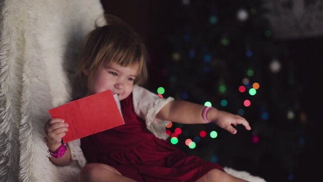 a child in red clothes is sitting waiting for the new year. the concept of celebrating Christmas at midnight. holiday costume. a girl writes a letter to Santa Claus. wish list