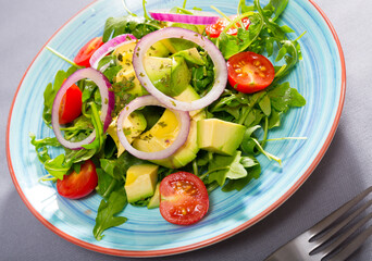 Fresh green arugula salad with chopped avocado, cherry tomatoes and red onion..