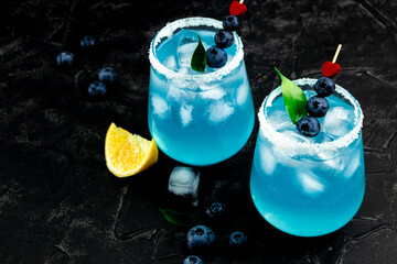  Two cocktails with ice, blue curacao and blueberries on a black background for valentine's day free space for text