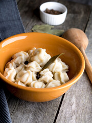 Boiled traditional Russian dumplings in ceramic dishes on a wooden table.