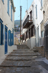 A narrow, winding street in a Mediterranean town with white walls, blue windows and stone steps.