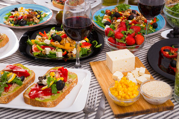 Delicious variety of vegetarian products and dishes with wine on striped fabric background .