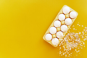 raw shell eggs pack flat lay illuminate yellow background, white sprind flowers, easter holiday
