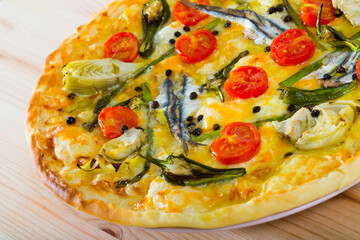 Pizza with sprat, artichokes, cheese and dried tomatoes on unleavened dough