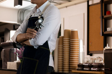 Young male Bartender in cafe restaurant. Smiling young waitress or small cafe business owner entrepreneur looking at camera, wear apron posing in restaurant coffeeshop. Barista making cappuccino.