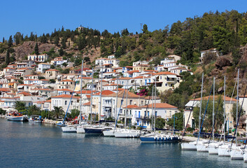 Fototapeta na wymiar An old Mediterranean town with white houses and red roofs on a mountainside. There are white boats in the port. The bright sky is reflected in the blue sea.