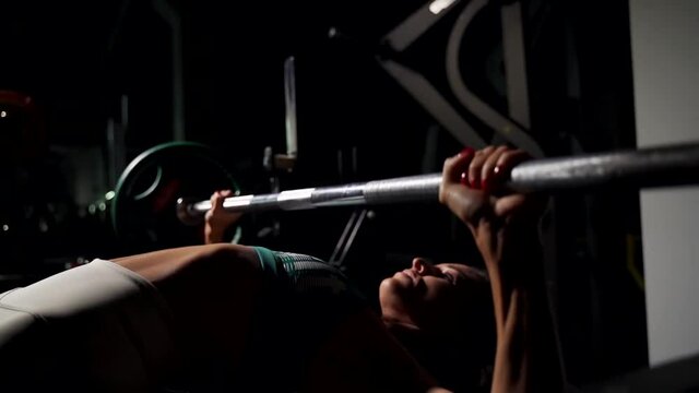 The girl in the gym lying on the bench raises the barbell from the chest.
