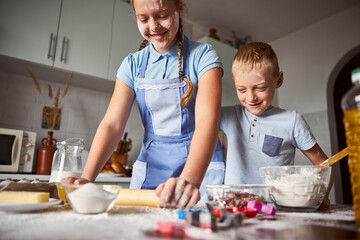 Joyous girl and boy preparing dough for baking