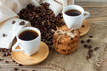 Two cups of freshly brewed espresso on wooden table. coffee beans and crunchie cookies on light...