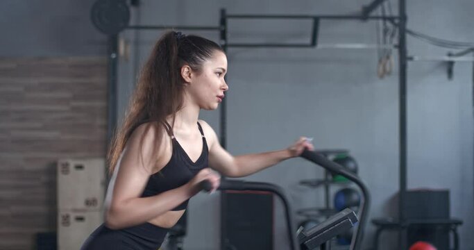 Female in the gym, young woman trains on a elliptical bike simulator, aerobic exercise and endurance training.