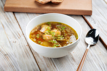 Side view on rich fish soup in a white bowl on the wooden table