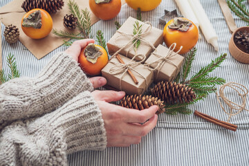 Obraz na płótnie Canvas The girl makes a new year composition of gifts Packed with her own hands in Kraft paper, top view, close-up. Happy Christmas background. Preparing for the holiday. Xmas concept