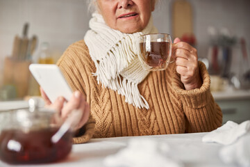 Sick senior woman looking at her phone and staying home