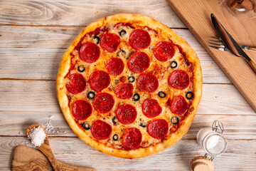 Top view on fresh baked pepperoni pizza with salami and olives on the wooden table