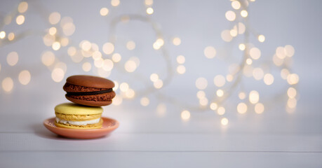 Multicolored French macaroons on a light background with a beautiful bokeh from a garland. Abstract background, selective focus