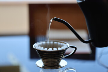 Barista making coffee with a pour over coffee maker in a dripper and pouring hot water from a black kettle
