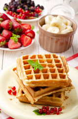 Stack of three belgian waffles on white kitchen table with strawberries bananas and red currant