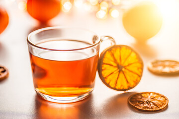 Glass cup of hot aromatic tea on white background with spices. Christmas tea with oranges on bokeh lights background. Christmas tea.
