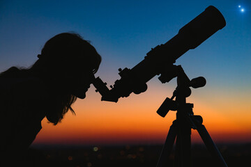 Woman looking at night sky with amateur astronomical telescope.